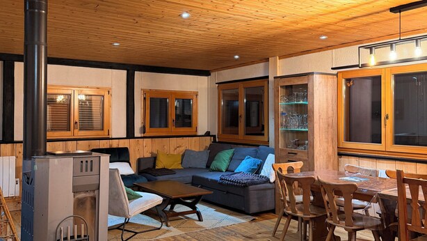 Una sala de estar acogedora con techo de madera, chimenea, sofá con cojines y una mesa de comedor con sillas.
