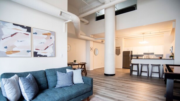 A modern living room with a blue sofa, a coffee table, and abstract wall art. - 5BR CozySuites The Block-SkybridgeAccess (Indianapolis)