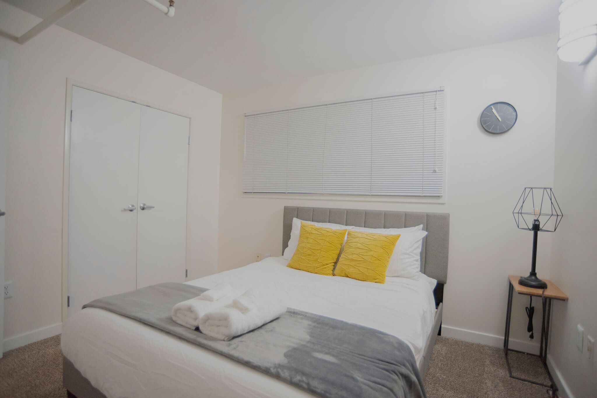 Une chambre à coucher avec un lit, une table de chevet avec une lampe, une fenêtre avec des stores et une porte.