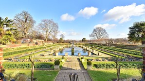 Un giardino formale con una fontana al centro, percorsi simmetrici e siepi curate.