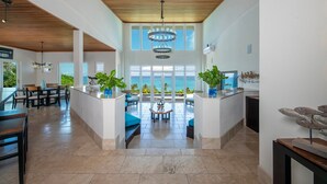 Een ruim, modern interieur met een hoge plafond, grote ramen met uitzicht op zee, en een centraal zithoek met een mooi vergezicht.