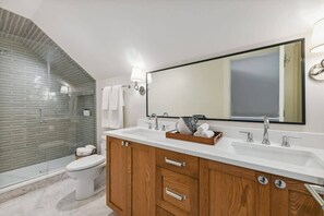 Un baño moderno con cabina de ducha de vidrio, inodoro blanco, armarios de madera y un espejo grande.