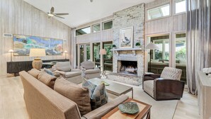 Ein geräumiges Wohnzimmer mit Kamin, gemütlicher Sitzgelegenheit und großen Fenstern.