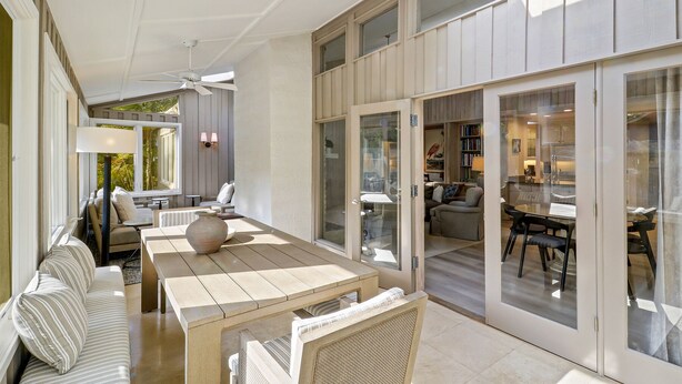 Ein großzügiger Patio-Bereich mit Esstisch, Stühlen und einer Couch. Eine Glasschiebetür führt zu einem angrenzenden Raum mit Küche und Sitzgelegenheit.