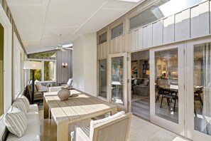 Un vaste patio comprenant une table à manger, des chaises et un canapé. Une porte-fenêtre coulissante donne accès à une pièce adjacente qui comprend une cuisine et un coin salon.