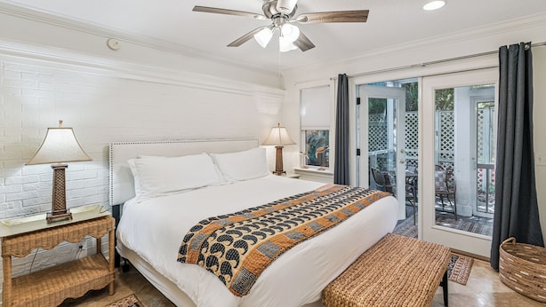 A bedroom with a bed, bedside lamps, a ceiling fan, and a view through a glass door to an outdoor area.