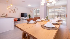 A modern kitchen with a wooden dining table set for a meal, a TV, and a sofa in the living area.