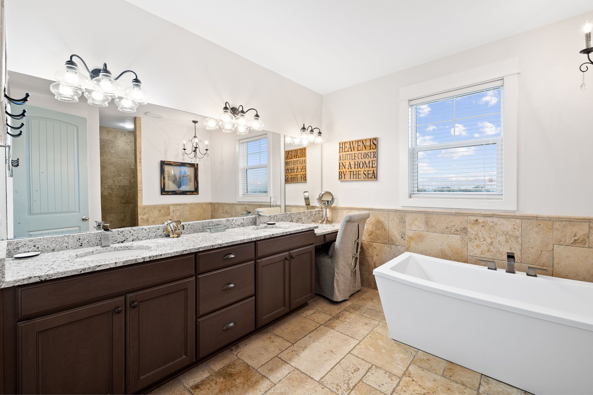 Une salle de bain moderne dotée d’un meuble-lavabo double, d’un grand miroir, d’une baignoire et offrant une vue sur la mer par la fenêtre.