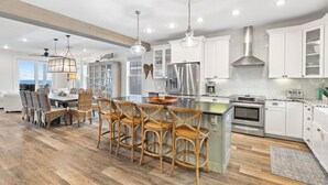 A modern kitchen with white cabinets, stainless steel appliances, and a central island with bar stools. - Family Beach Retreat w/Pool and Elevator (Port St. Joe)