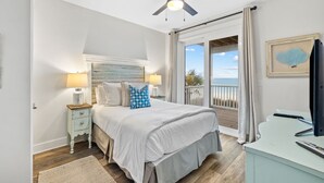 A bedroom with a bed, nightstand, lamp, ceiling fan, and a view of the ocean through a sliding door. - Family Beach Retreat w/Pool and Elevator (Port St. Joe)