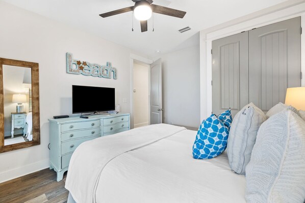 A bedroom with a bed, a dresser, a television, a ceiling fan, and a wardrobe.