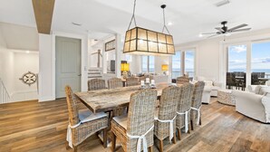 A spacious living room with a large dining table, wicker chairs, a ceiling fan, and large windows offering a view. - Family Beach Retreat w/Pool and Elevator (Port St. Joe)