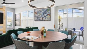 Un comedor moderno con una mesa redonda, sofás tapizados en verde y un cuadro abstracto grande en la pared.