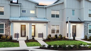 A modern multi-story residential building with a stone facade, multiple entryways, and a well-maintained lawn.