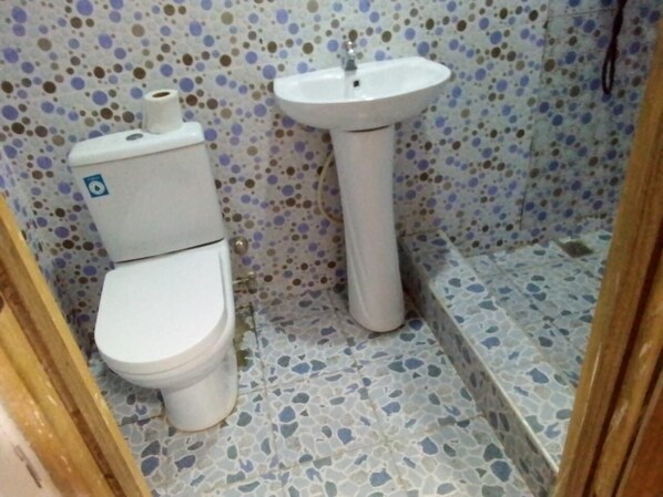Un baño pequeño con inodoro y lavamanos pedestal. El suelo tiene un estampado de baldosas con motas.
