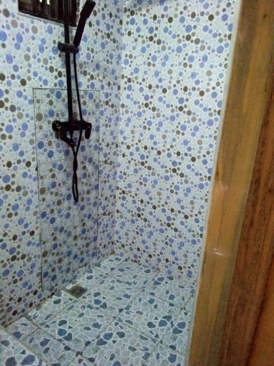 A bathroom with a tiled floor and walls, a shower area, and a wooden door.