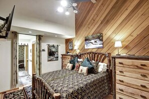 A bedroom with a wooden ceiling, a bed with patterned bedding, a dresser, and a painting on the wall. - Snowcreek 464- Nice Condo with Mountain Views (Mammoth Lakes)