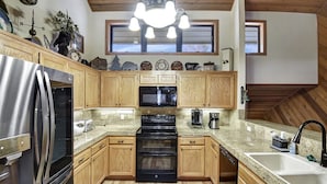 A kitchen with wooden cabinets, a stainless steel refrigerator, a black oven, a coffee maker, and a window above the sink.