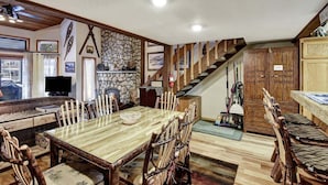 A spacious dining area with a large wooden table and chairs, a stone wall, and a staircase leading to upper levels.