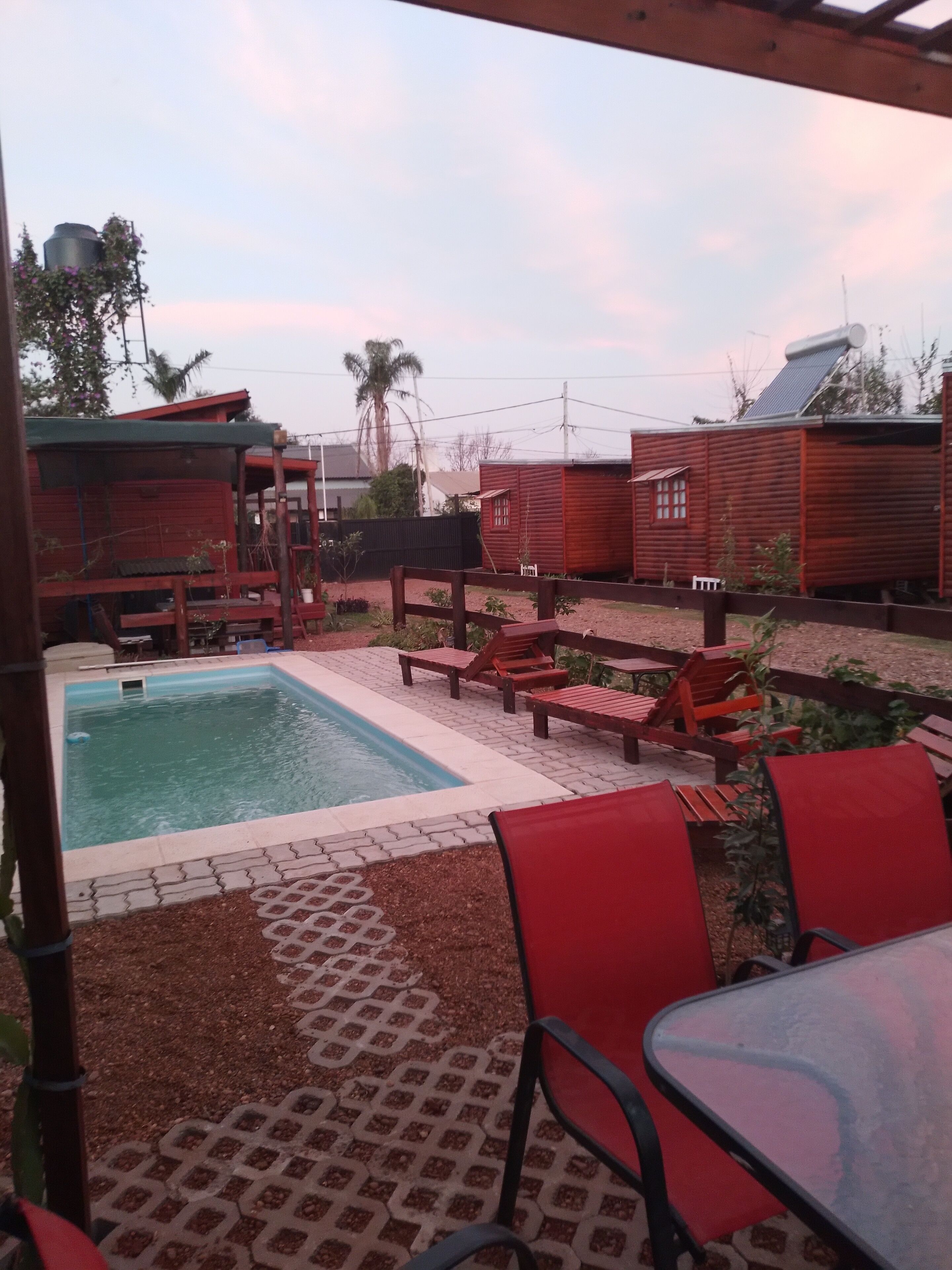 Un área de piscina con suelo de baldosas, sillas de descanso rojas y una pileta pequeña.