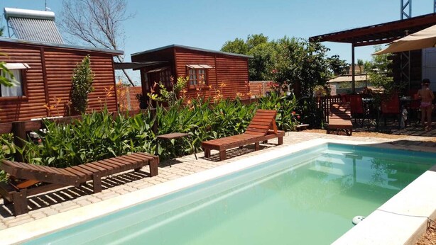 Un área de piscina con sillones de madera y una pequeña construcción.