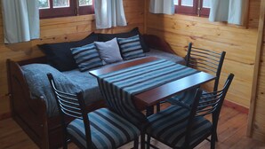 Un interior acogedor de cabaña con suelo de madera, un sofá con cojines a rayas, una mesa de madera y dos sillas.