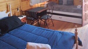 Una habitación de cabaña de madera con una cama, una mesa con sillas, un ventilador de techo y una ventana con cortinas.