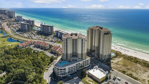 An aerial view of a coastal area with a hotel featuring a rooftop pool, adjacent to a beach and ocean. - Gulf-view balcony w/ hot tub & beach access (Panama City Beach)
