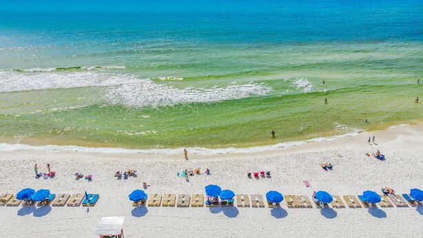 A beach with rows of sun loungers and umbrellas, a sandy shore, and the ocean in the background. - Gulf-view balcony w/ hot tub & beach access (Panama City Beach)