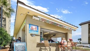 An outdoor bar with a chalkboard menu, outdoor seating, and a clear sky. - Gulf-view balcony w/ hot tub & beach access (Panama City Beach)