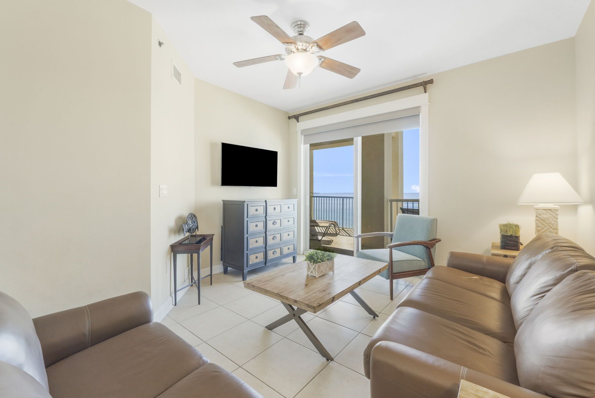 Ein Wohnzimmer mit Deckenventilator, einem Flachbildfernseher, einer Couch, einem Couchtisch und Blick auf den Balkon.