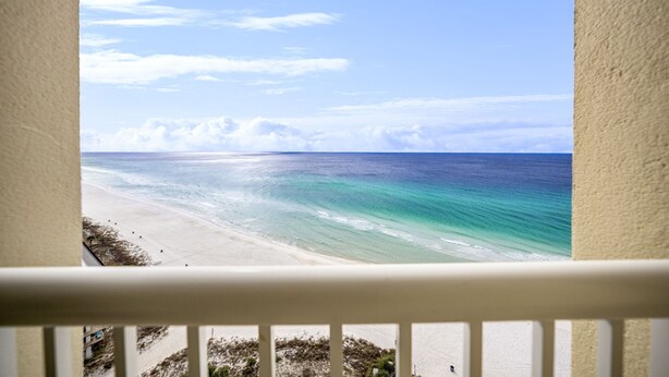 Une vue depuis un balcon sur une plage, avec un ciel dégagé et une mer calme.