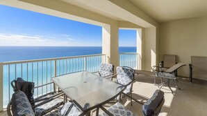 A balcony with a glass table and chairs, overlooking a clear blue sea.
