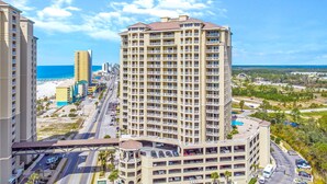 A high-rise hotel with multiple balconies, a parking garage, and a view of the beach and ocean.