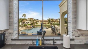 A kitchen with a large window overlooking a pool and outdoor seating area.