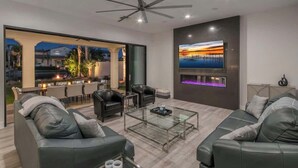 A modern living room with a glass coffee table, leather sofas, and a ceiling fan.
