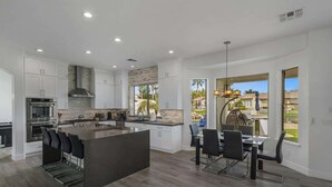 A modern kitchen with white cabinetry, a large island, and a dining area with a view of the outdoors.