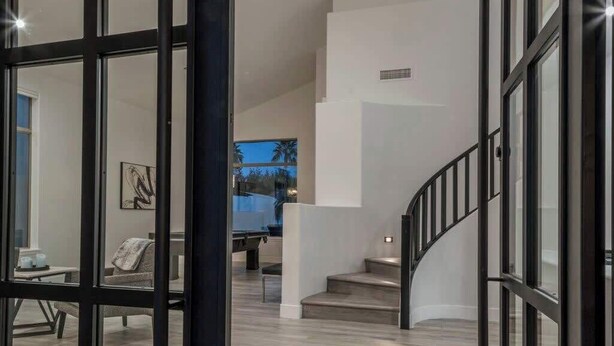 A spacious interior with a modern staircase, a unique circular light fixture, and a view of the outdoors through large windows.