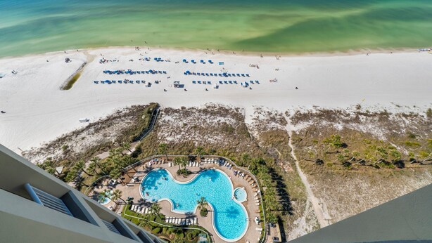 Vue aérienne d’un complexe hôtelier doté d’une grande piscine, d’une plage et d’une eau d’un bleu cristallin.