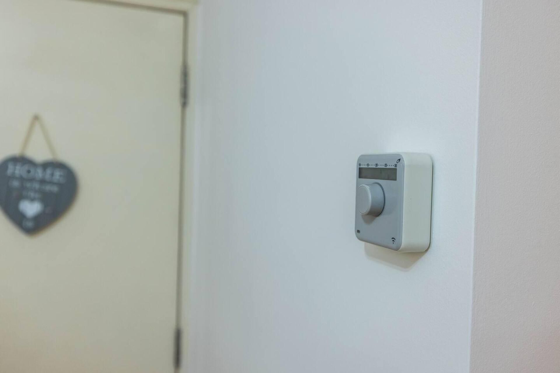 A thermostat on a wall, a door, and a heart-shaped decoration with the word "HOME" on it.