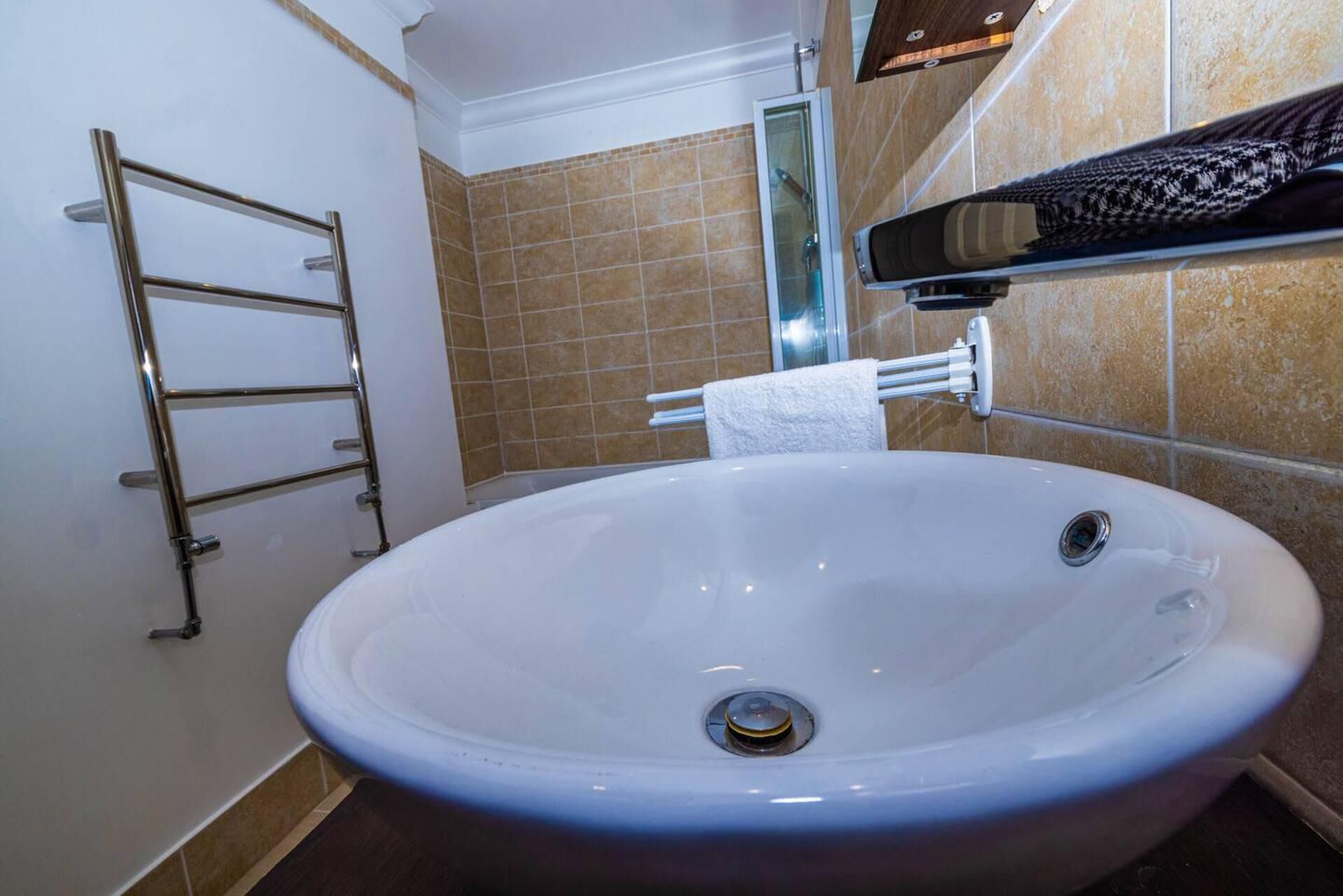 A bathroom with a large white sink, a towel rack, and a glass shower enclosure.