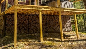 Une cabane avec des fondations en pierre, une terrasse en bois et une grande fenêtre.