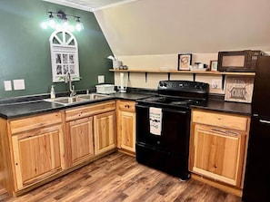 A kitchen with wooden cabinets, a black stove, a microwave, and a sink. - Rustic Cabin Retreat Near RRG & Cave Run (Wellington)