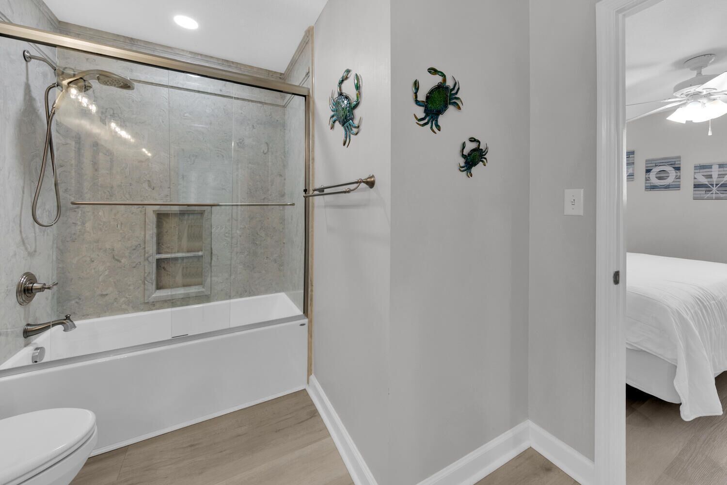A modern bathroom with a glass-enclosed shower, a bathtub, and a toilet. There are decorative crab wall art pieces.