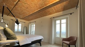 A bedroom with a brick ceiling, a bed with white linens, a bedside table with a lamp, a chair, and a window with a view. - Luxury home with pool and spectecular views (Piemonte)