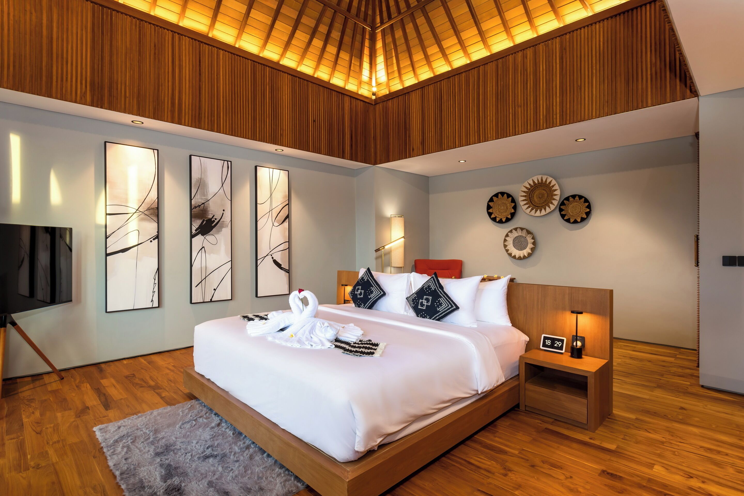 A modern hotel room with a large bed, wooden ceiling, and wall-mounted artwork.