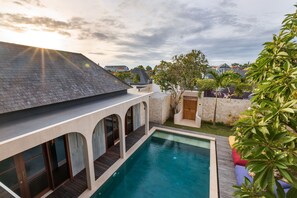 A modern house with a swimming pool, arched windows, and a stone wall. - Navya Villas (Kerobokan)