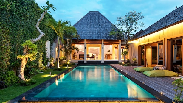 A modern house with a swimming pool, wooden deck, and lush greenery. - Navya Villas (Kerobokan)
