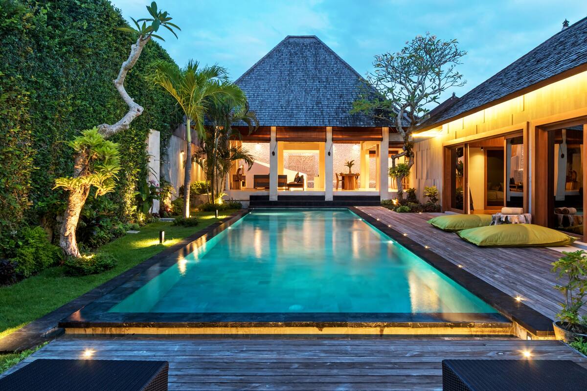 A modern house with a swimming pool, wooden deck, and lush greenery.
