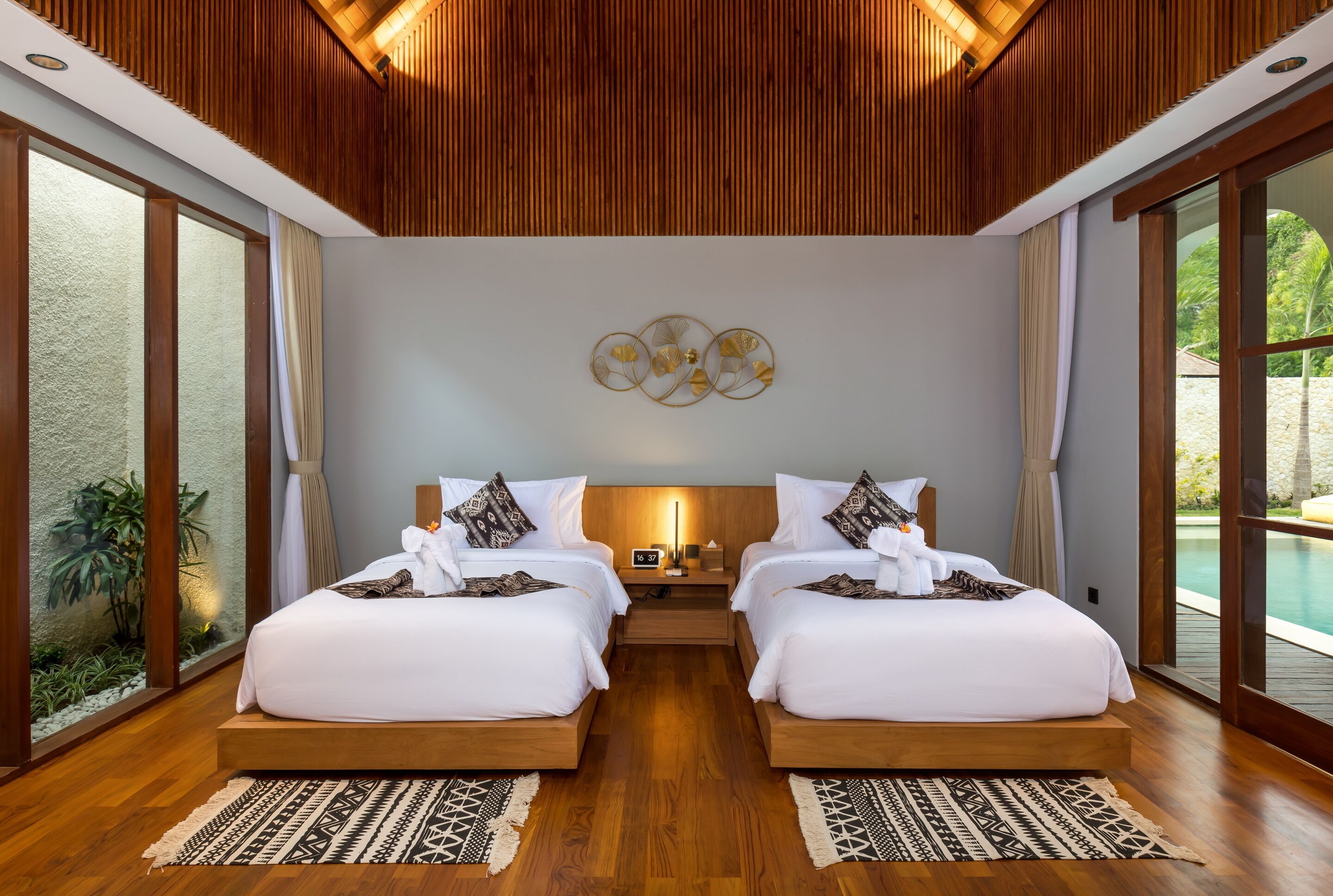 A double room with two beds, a wooden ceiling, a large window, and a wall-mounted artwork.